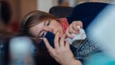Suspected COVID Case: A sick woman lies on the sofa holding a smartphone in her hand.