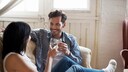 A young couple sits on the sofa, drinking white wine.