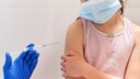 A girl wearing a face mask receives a vaccination in her arm.