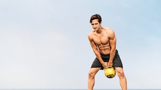 Young, fit man does kettlebell swing on the beach