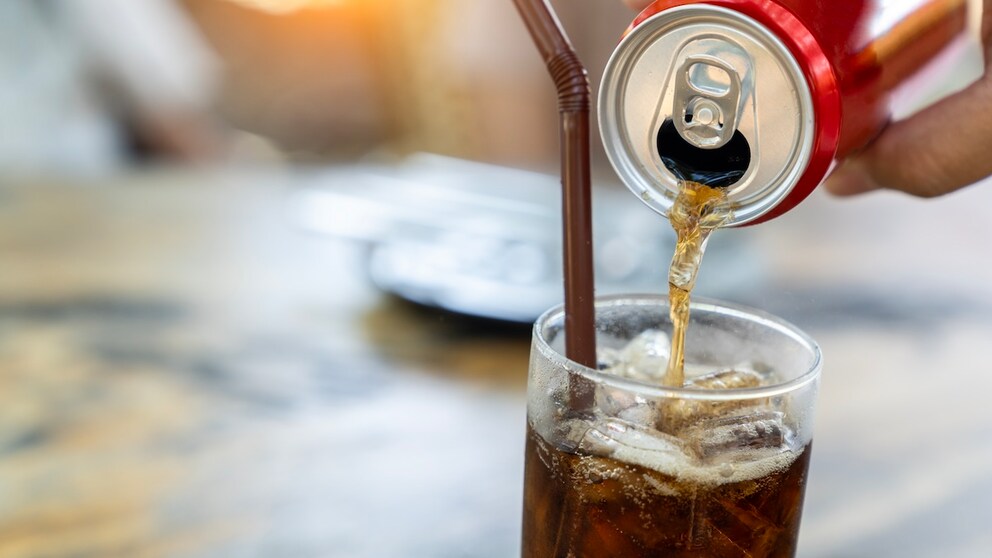 Someone fills a glass with a soft drink.