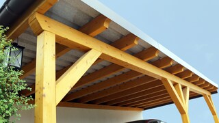 A car is parked under a wooden carport.