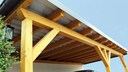 A car is parked under a wooden carport.