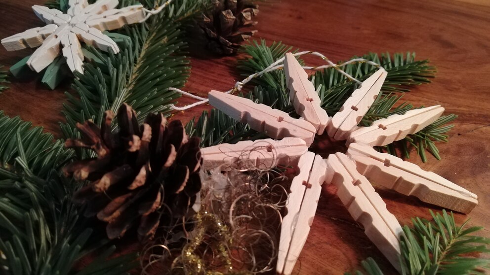 Christmas stars made from clothespins are placed on a table among pine greenery and cones.