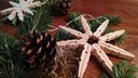 Christmas stars made from clothespins are placed on a table among pine greenery and cones.