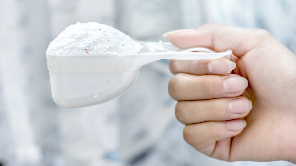 A hand holds washing powder in a ladle