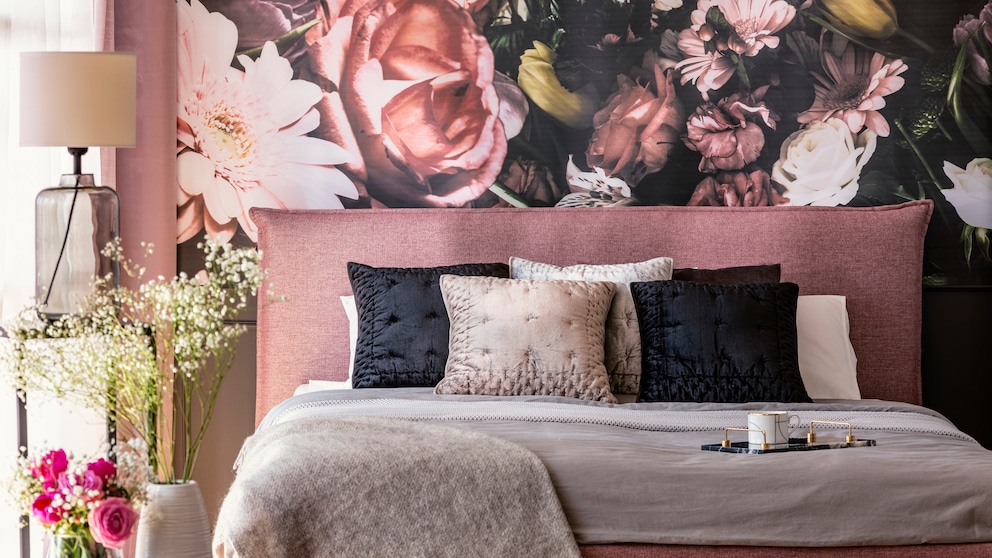 A bed rich in textiles in dusty pink set against wallpaper featuring a lush floral bouquet