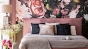 A bed rich in textiles in dusty pink set against wallpaper featuring a lush floral bouquet
