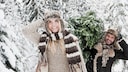 Cutting Your Own Christmas Tree: A Couple Smiles as They Carry a Christmas Tree Through a Winter Snow Landscape