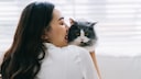 A young woman holds a cat that she doesn't like.