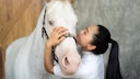 Woman kisses white horse on head