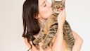 Young woman holds a cat in her arms and gives it a kiss