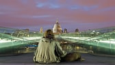 A homeless man and his dog at night on the Millennium Bridge with St. Paul's Cathedral in the background.