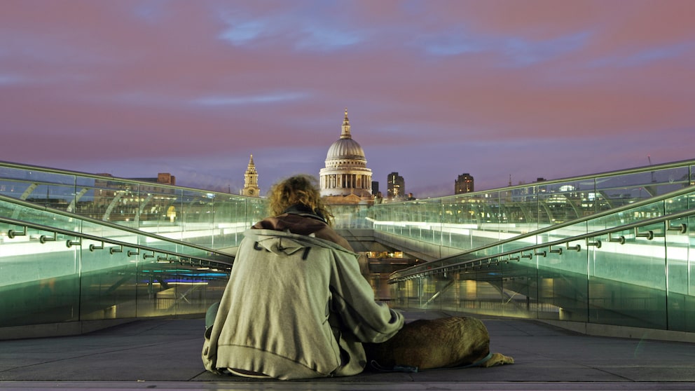 A homeless man and his dog at night on the Millennium Bridge with St. Paul's Cathedral in the background.