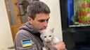 A small white cat perches traumatized on the arm of a soldier