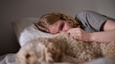 A crying young woman lies in bed next to her dog