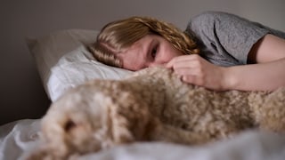 A crying young woman lies in bed next to her dog