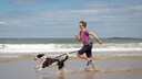 Young woman and dog run together on the beach