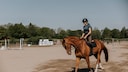Woman horse riding on paddock at sunny day