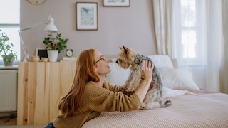 Smiling woman holding a Yorkshire Terrier sitting on the bed