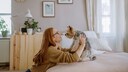 Smiling woman holding a Yorkshire Terrier sitting on the bed