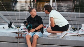 Two people arguing on a boat dock. A dog sits on the lap of the person on the left.