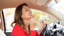 Mature woman in a car, laughing as she adjusts her lipstick.