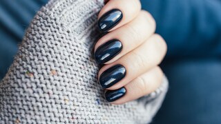 Woman's hand with dark blue nail polish and gray knitted sweater