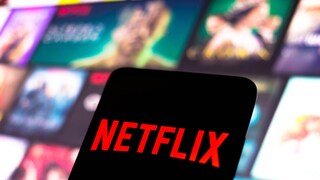 Netflix logo on a phone, with streaming tiles in the background.