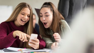Two young women look at a smartphone and use chat abbreviations.