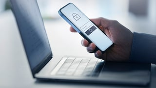 Two-Factor Authentication (2FA) Stock Image: Man holding smartphone with lock icon in front of laptop