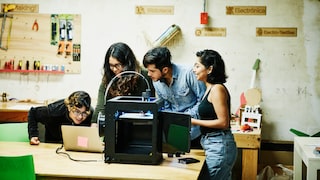 Four people stand in front of a 3D printer and a laptop.