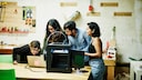 Four people stand in front of a 3D printer and a laptop.