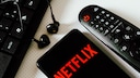 Netflix Account Sharing Fee Consequences: Netflix Logo on Smartphone Next to Remote Control and Computer Keyboard