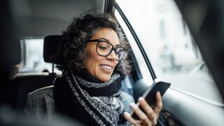 A woman looks at her smartphone in her hand while driving.