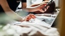 Stock Image: Woman holding smartphone and typing on laptop
