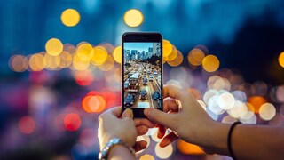 Symbolic image: Woman takes a photo of evening traffic with a smartphone, which can be seen in the background with a bokeh effect.