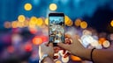 Symbolic image: Woman takes a photo of evening traffic with a smartphone, which can be seen in the background with a bokeh effect.