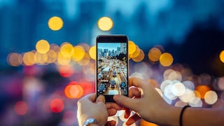 Symbolic image: Woman takes a photo of evening traffic with a smartphone, which can be seen in the background with a bokeh effect.