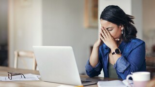 A woman working from home covers her face with her hands due to an error message on her laptop.