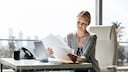 Woman with a lot of paperwork in front of the laptop.