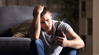 Stock photo: Young man looks worriedly at his smartphone.