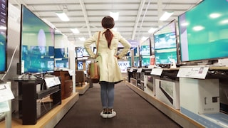 A woman stands in front of many televisions.