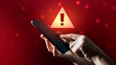 Malware Stock Image: Hand holding a smartphone with a large warning sign in the background