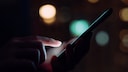 SIM Swapping Symbolic Image: a glowing phone held in a hand in the dark