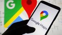 A person holds a phone with the Google Maps logo on the display, with the app open in the background.