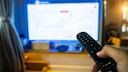A person points a remote control at a television.