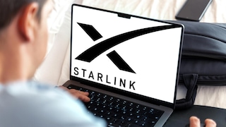 A man sits in front of a laptop displaying the Starlink logo.