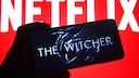 "The Witcher" logo on a smartphone, with a Netflix sign in the background.