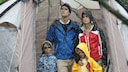 Family Stands Unhappily in a Tent in the Rain